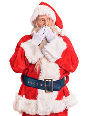 Old senior man with grey hair and long beard wearing traditional santa claus costume laughing and embarrassed giggle covering mouth with hands, gossip and scandal concept