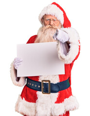 Old senior man with grey hair and long beard wearing santa claus costume holding banner pointing...