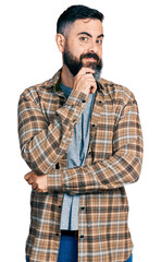 Hispanic man with beard wearing casual shirt looking confident at the camera with smile with crossed arms and hand raised on chin. thinking positive.