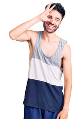 Young hispanic man wearing casual clothes doing ok gesture with hand smiling, eye looking through fingers with happy face.