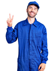 Young hispanic man wearing painter uniform smiling with happy face winking at the camera doing...
