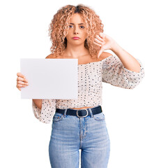 Young blonde woman with curly hair holding sale poster with angry face, negative sign showing...