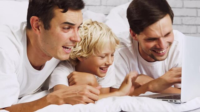 Lgbt family, gay couple with adopted son. Happy modern family spending time together at home and watching movies on the laptop