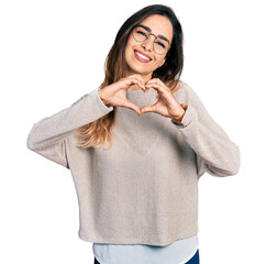 Beautiful hispanic woman wearing casual sweater and glasses smiling in love doing heart symbol...