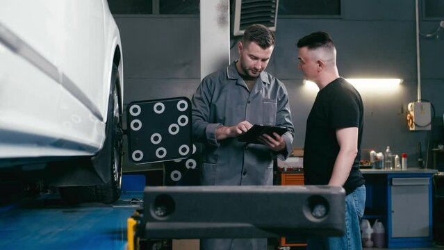 A car service employee installs a wheel adapter with a target on the wheel to perform a wheel alignment. Diagnostics and balancing of wheels of a lifting trolley at a modern service station.