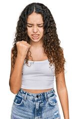 Teenager hispanic girl wearing casual clothes angry and mad raising fist frustrated and furious while shouting with anger. rage and aggressive concept.