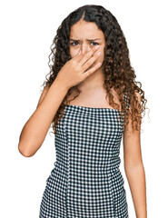 Teenager hispanic girl wearing casual clothes smelling something stinky and disgusting, intolerable smell, holding breath with fingers on nose. bad smell