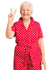 Senior beautiful woman with blue eyes and grey hair wearing a red summer dress showing and pointing up with fingers number two while smiling confident and happy.