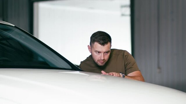 Professional inspector in the repair service. A male mechanic in uniform stands in a repair shop and inspects a car after straightening and painting