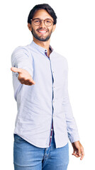 Handsome hispanic man wearing business shirt and glasses smiling cheerful offering palm hand giving...