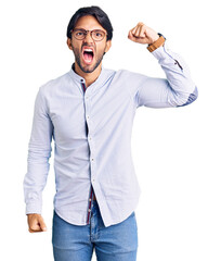 Fototapeta premium Handsome hispanic man wearing business shirt and glasses angry and mad raising fist frustrated and furious while shouting with anger. rage and aggressive concept.