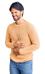 Handsome hispanic man wearing casual sweater with hand on stomach because nausea, painful disease feeling unwell. ache concept.