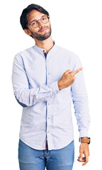 Fototapeta premium Handsome hispanic man wearing business shirt and glasses pointing with hand finger to the side showing advertisement, serious and calm face