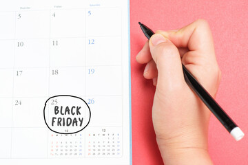 Female hand writes in the calendar Black friday on a red background close-up, top view.