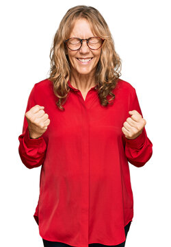 Middle age blonde woman wearing casual shirt over red background very happy and excited doing winner gesture with arms raised, smiling and screaming for success. celebration concept.