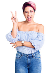 Young beautiful woman with pink hair wearing casual clothes smiling with happy face winking at the camera doing victory sign with fingers. number two.