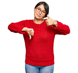 Young beautiful hispanic woman with short hair wearing casual sweater and glasses doing thumbs up...