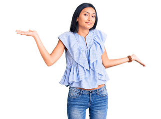 Young beautiful latin girl wearing casual clothes clueless and confused expression with arms and hands raised. doubt concept.