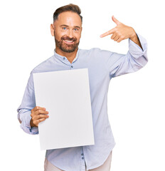 Handsome middle age man holding blank empty banner pointing finger to one self smiling happy and proud