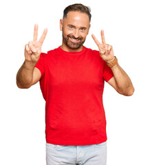Fototapeta premium Handsome middle age man wearing casual red tshirt smiling looking to the camera showing fingers doing victory sign. number two.