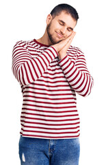 Young handsome man wearing striped sweater sleeping tired dreaming and posing with hands together while smiling with closed eyes.