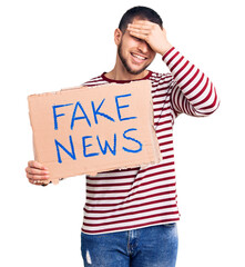 Young handsome man holding fake news message banner stressed and frustrated with hand on head,...