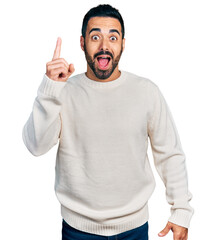 Young hispanic man with beard wearing casual white sweater pointing finger up with successful idea. exited and happy. number one.