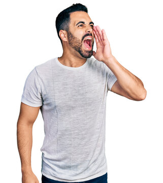 Young hispanic man with beard wearing casual grey t shirt shouting and screaming loud to side with hand on mouth. communication concept.