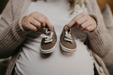 Expectant mother holding up cute baby shoes 