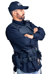Young hispanic man wearing police uniform looking to the side with arms crossed convinced and confident