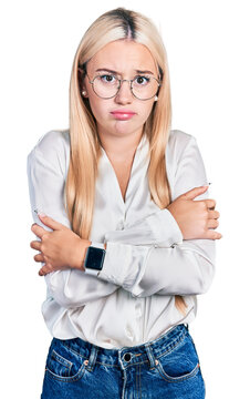 Beautiful blonde woman wearing elegant shirt and glasses shaking and freezing for winter cold with sad and shock expression on face