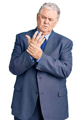 Senior grey-haired man wearing business jacket suffering pain on hands and fingers, arthritis inflammation