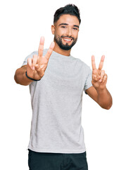 Young man with beard wearing casual grey tshirt smiling looking to the camera showing fingers doing victory sign. number two.