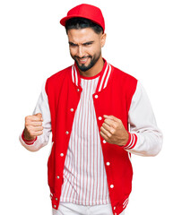 Young man with beard wearing baseball uniform excited for success with arms raised and eyes closed celebrating victory smiling. winner concept.