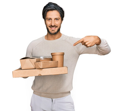 Young hispanic man holding take away food pointing finger to one self smiling happy and proud
