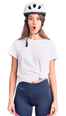 Young beautiful girl wearing bike helmet scared and amazed with open mouth for surprise, disbelief face