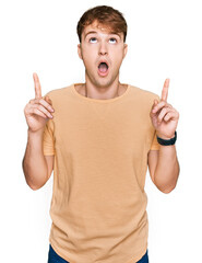 Young caucasian man wearing casual clothes amazed and surprised looking up and pointing with fingers and raised arms.