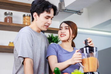 Obraz premium Asian young romantic lover couple handsome husband standing smiling hugging beautiful wife from behind while using blender blending preparing mixed fresh raw organic fruits juice on kitchen counter