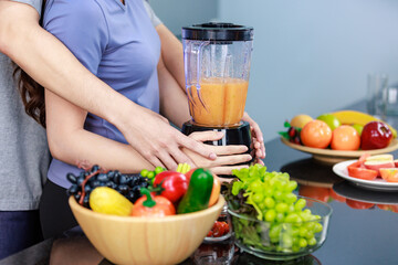 Closeup shot of hands holding of unrecognizable unknown romantic lover couple while female model using blender blending orange juice on kitchen counter full of fresh organic fruits and vegetables