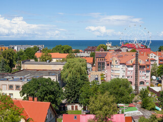 Summer view of tiled roofs, streets with people and ferris wheel ride