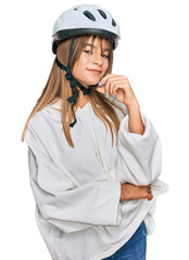 Teenager caucasian girl wearing bike helmet looking confident at the camera with smile with crossed arms and hand raised on chin. thinking positive.