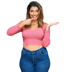 Beautiful brunette woman wearing casual clothes amazed and smiling to the camera while presenting with hand and pointing with finger.