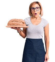 Young blonde woman holding wholemeal bread scared and amazed with open mouth for surprise, disbelief face