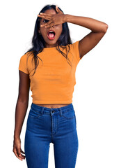 Fototapeta premium Young indian girl wearing casual clothes and glasses peeking in shock covering face and eyes with hand, looking through fingers with embarrassed expression.