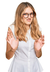 Beautiful young caucasian girl wearing casual clothes and glasses disgusted expression, displeased and fearful doing disgust face because aversion reaction. with hands raised