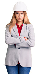 Beautiful young woman wearing architect hardhat skeptic and nervous, disapproving expression on face with crossed arms. negative person.