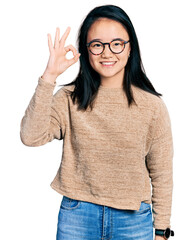 Young chinese woman wearing casual sweater and glasses smiling positive doing ok sign with hand and fingers. successful expression.