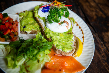Healthy avocado toast on gluten free bread with poached eggs and green salads with tomatos on white plate in cafe.