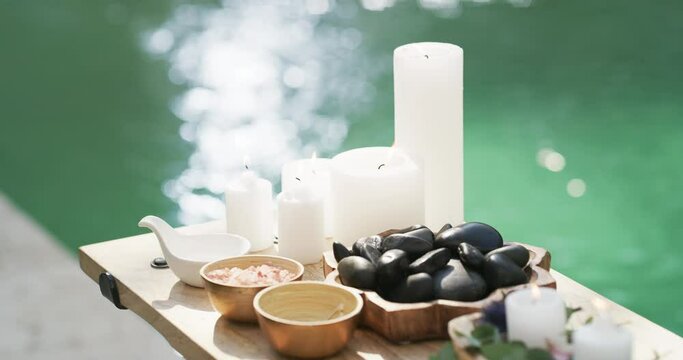 Massage, stone and candle in a spa to relax for health and wellness in a beauty club and water in the background. Peace, luxury or skincare with aromatherapy by the pool for healthy and holistic care