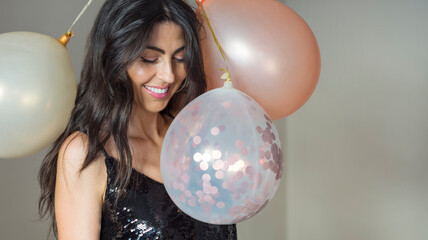 Fototapeta premium Beautiful woman in black shiny dress holding party balloons and smiling . Portrait with copy space 